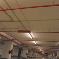 V garážích jsou červeně lakované potrubní rozvody SHZ nepřehlédnutelné. Dobře jsou vidět mechanické spoje potrubí i sprinklerové hlavice.