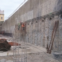 Pohled na pilotovou stěnu ze stavební jámy při dokončování finálního povrchu ze stříkaného betonu. Jasně je viditelná spodní úroveň kotvení.